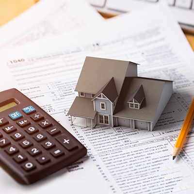 a house model, a calculator, and a pencil on a stack of documents