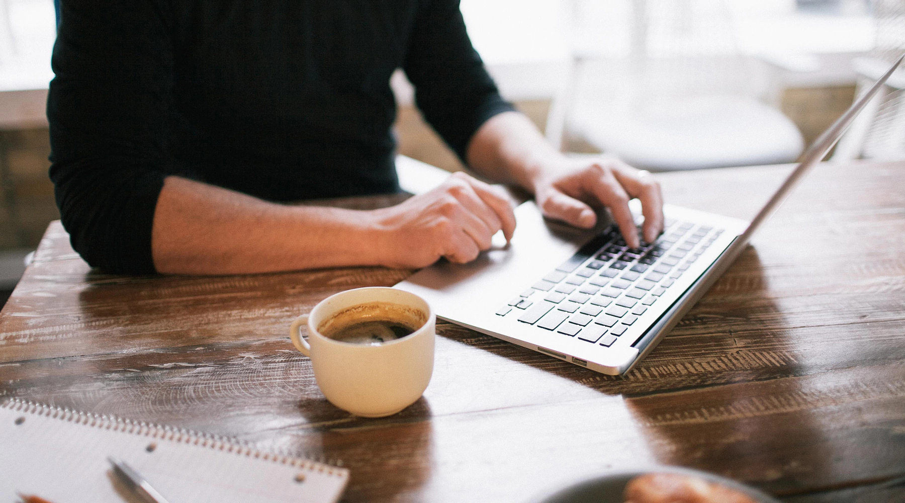 a gentleman using his laptop enjoying SC banking services, with a coffee on the desk
