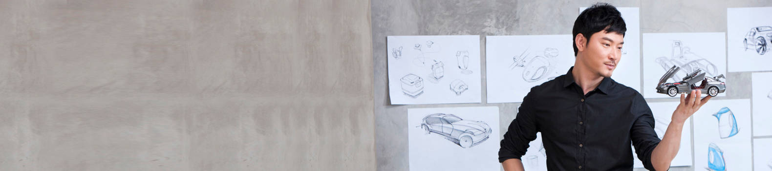 a gentleman in black shirt holding a silver car model, with designs blueprints on the wall