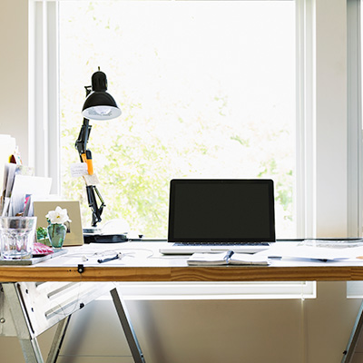 a working desk with lamps, laptop, notebook, and blueprints, by the window.