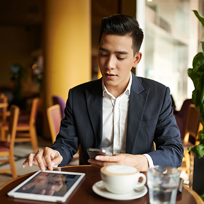 a gentleman checking on Straight2Bank platform with mobile phone and tablet, in a cafe