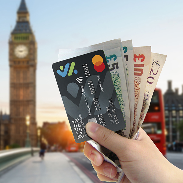 A hand holding a Multi-Currency Mastercard Debit Card and foreign currency against London scenery