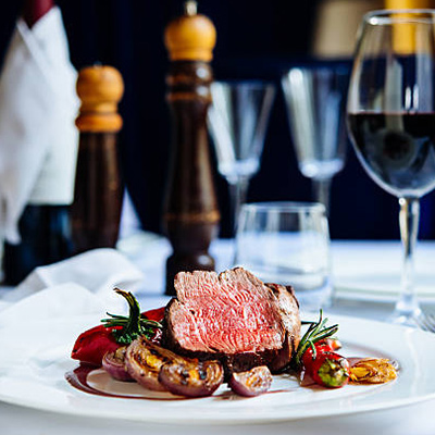 a medium rare steak dish, containers with seasoning, and glass of wine