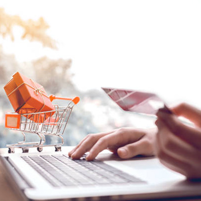 a person holding a credit card while using laptop; gift box in shopping cart model beside