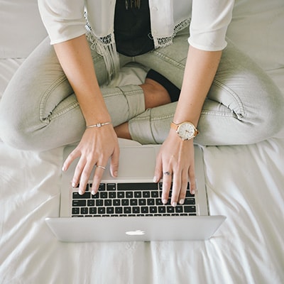 a lady with jeans using her laptop to apply banking service online on bed