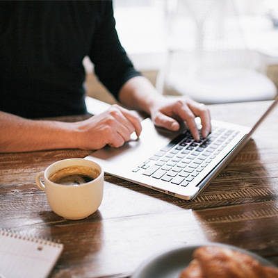 a gentleman using a laptop for SC online services, with a dark coffee on a desk.